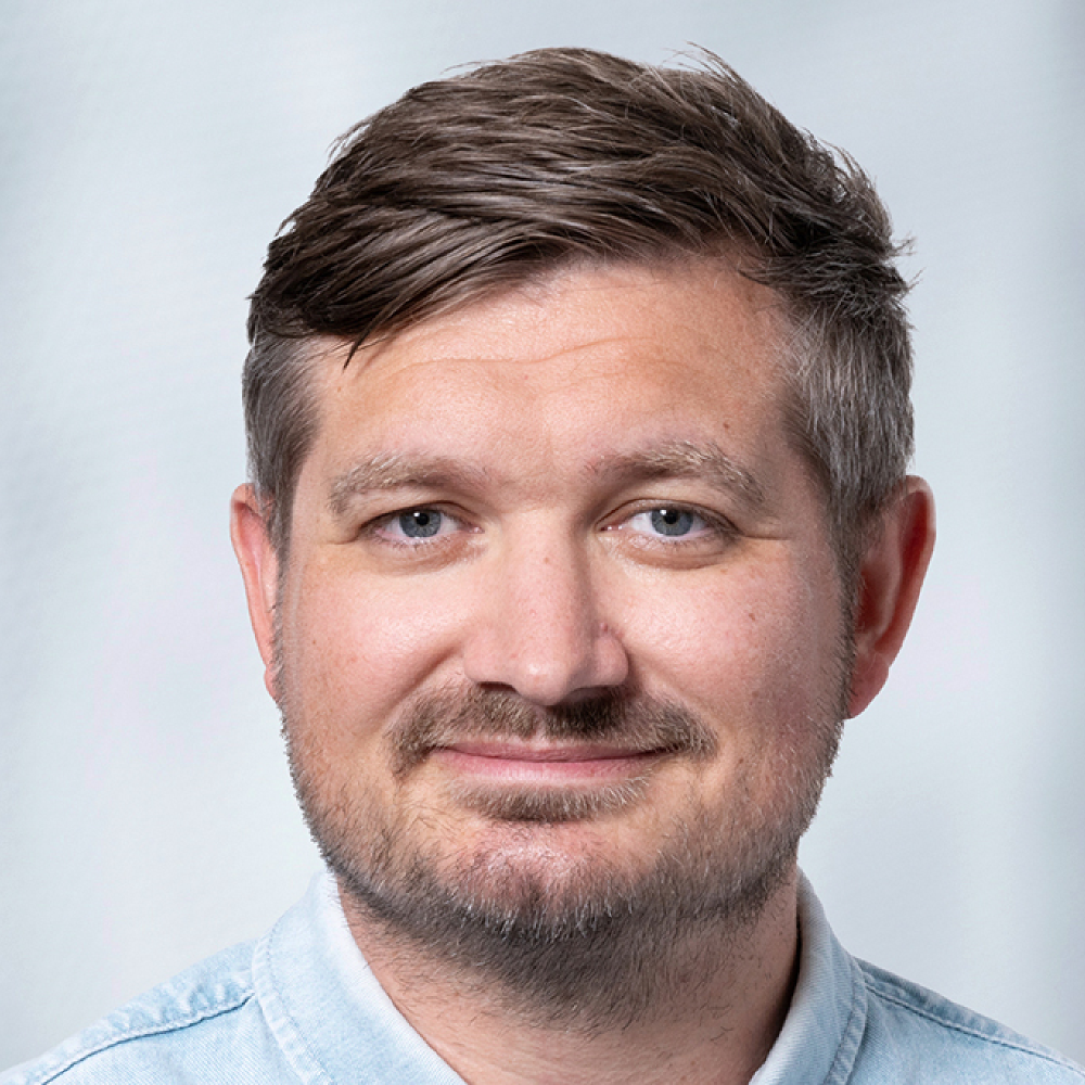 Portrait of Benjamin Börner, male, white person wearing short hair, a beard, and a light blue shirt.