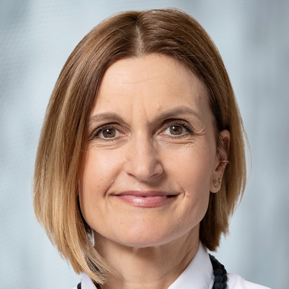 Portrait of Karin Gilland Lutz, female, white person with medium-length hair, black necklace, and white shirt