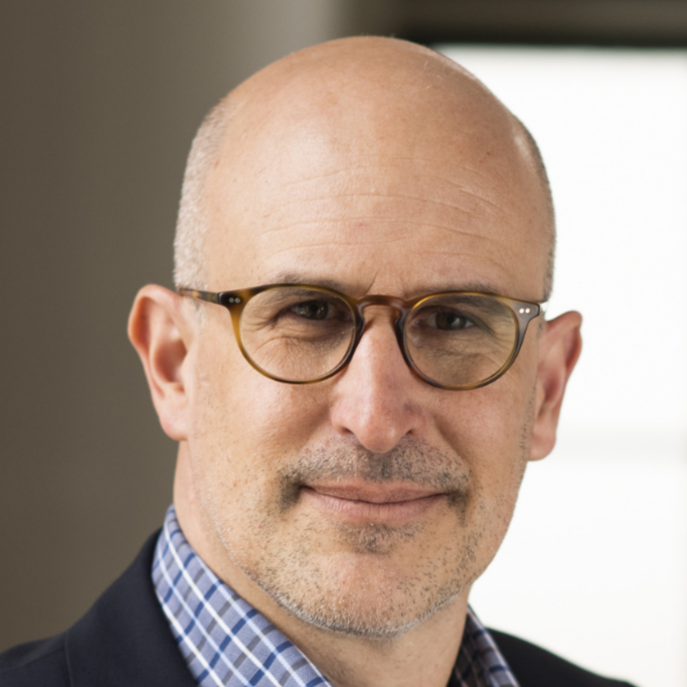 Portrait of Prof. Dr. Matthias D. Wüthrich, male, light-skinned person wearing a blue-checked shirt, black blazer, glasses, and a glaze