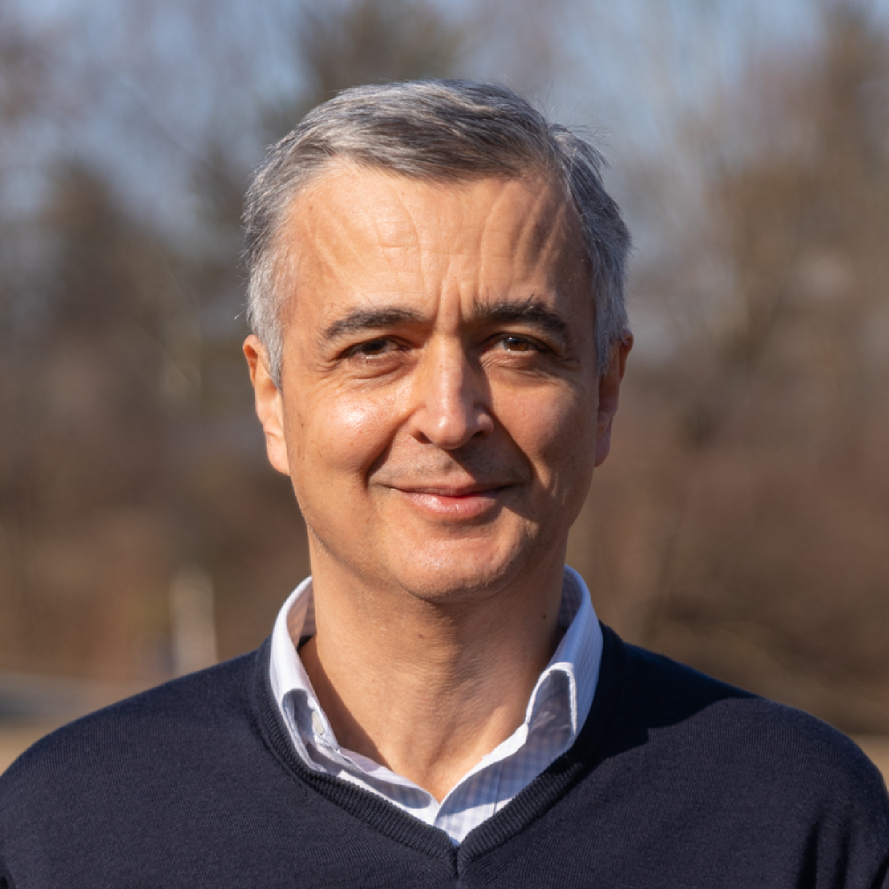 Portrait of Prof. Dr. Amadeo Caflisch, male, light-skinned person wearing a light-colored shirt collar under a blue sweater and short gray-white hair.
